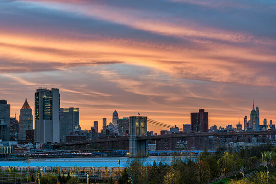 A tranquil cityscape with a colorful sunset behind a bridge and modern skyscrapers. New York City, NY, USA