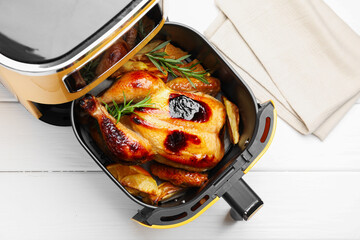 Tasty grilled chicken with rosemary and vegetables in air fryer on white wooden table, top view