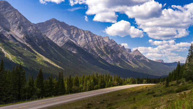 Majestic mountain range with a scenic road winding through lush green forests below. Kananaskis, Alberta, Canada