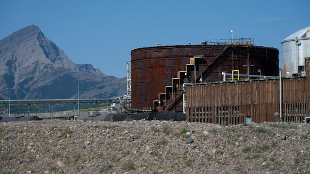 Industrial storage tanks and pipelines with a mountain backdrop under a clear blue sky. Pincher Creek, Alberta, Canada