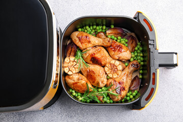 Air fryer with grilled chicken drumsticks, spices and green peas on grey table, top view