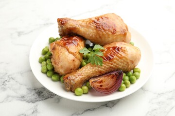 Grilled chicken drumsticks, green peas, onion and parsley on white marble table, closeup