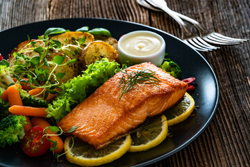 Fried salmon steak with boiled broccoli and mini carrots, fried potatoes and mayonnaise on wooden...