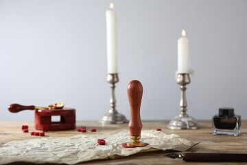 Old paper scroll, inkwell, pieces of wax, stamp and burning candles on wooden table, closeup