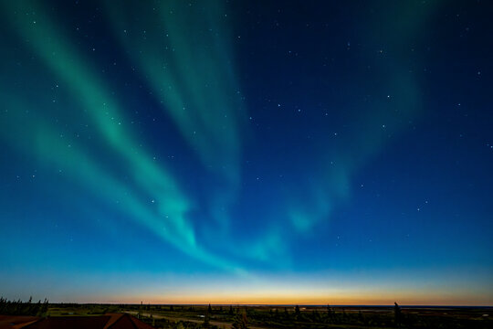 Northern lights with green auroras dancing in a clear night sky over a tranquil landscape. Hudson Bay, Churchill, Manitoba, Canada