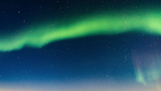 A vivid green aurora borealis arcs across a starlit night sky. Hudson Bay, Churchill, Manitoba, Canada