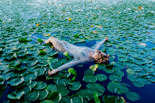 Woman in white lace dress floating on a lily-covered pond with a floral headband. Wildcat Lake Park, WA, USA