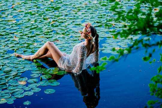 Woman in flower crown relaxes in a lily pond wearing a white lace outfit. Wildcat Lake Park, WA, USA