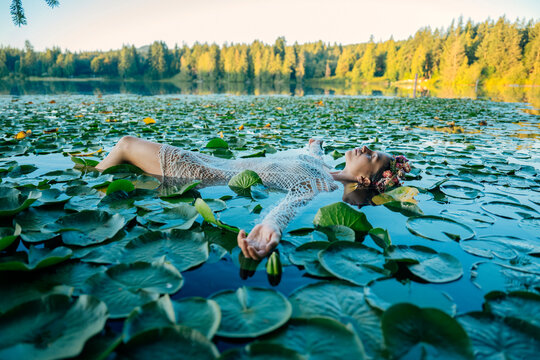Woman in a white dress floating on a serene lily pad-covered lake under a clear sky. Wildcat Lake Park, WA, USA