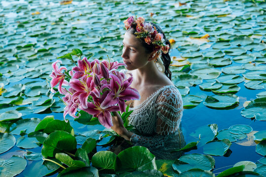 Woman in water with flower crown holding pink lilies surrounded by lily pads. Wildcat Lake Park, WA, USA