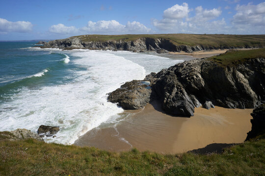 Porth Joke Beach, also known as Polly Joke, near Newquay, Cornwall, UK. Rugged coastline with waves crashing onto sandy beaches under a partly cloudy blue sky.
