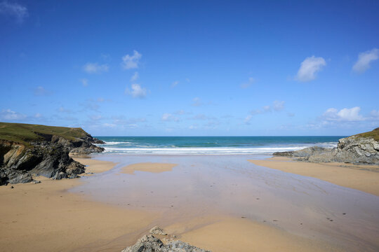 Porth Joke Beach, also known as Polly Joke, near Newquay, Cornwall, UK. A serene, empty beach with blue skies, gentle waves, and rocky cliffs in the background.