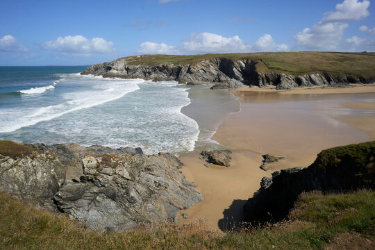Rocky coastline with waves crashing and sandy beach under a clear blue sky.