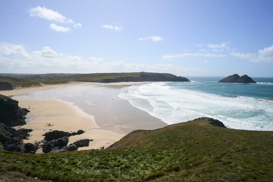 Holywell Bay and beach, Cornwall, UK. Expansive beach with waves, rocky shoreline, and clear blue sky on a sunny day.
