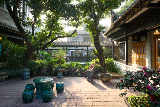Guangzhou, China. A courtyard in Liwan district, near Liwan lake. Sunlit traditional courtyard garden with lush greenery and decorative ceramic stools.