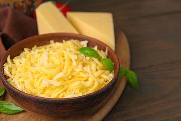 Grated and pieces of cheese with basil on wooden table, closeup