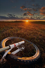 A bicycle wheel against the background of a meadow and a bright sunset sky with the sun. Travel and adventure