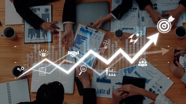 A team of business professionals collaborates around a table analyzing charts and data to devise strategies for growth and enhanced performance in a dynamic workspace. Raster