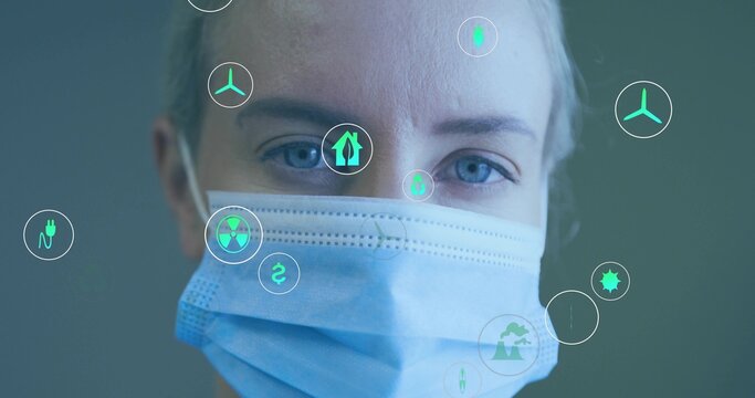 Mid-adult researcher wearing surgical mask analyzing floating energy and eco icons in clinic - Powered by Adobe