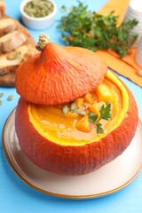 Tasty pumpkin cream soup with seeds and parsley served in pumpkin on light blue wooden table, closeup