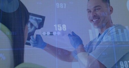 Male dentist wearing gloves holding dental imaging strip in operatory, with x-ray monitor and bib