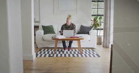Man wearing plaid shirt typing on laptop and checking smartphone on coffee table in living room