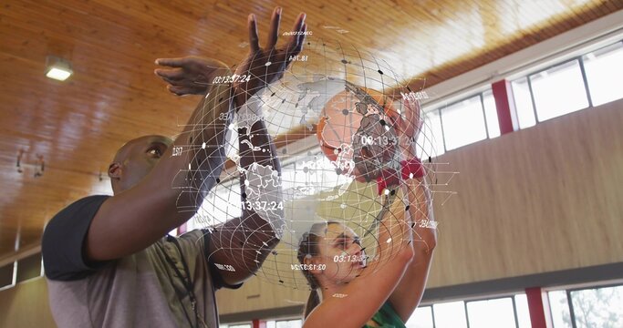 Coach guiding adult female in green jersey shooting basketball in wooden gym, with red columns
