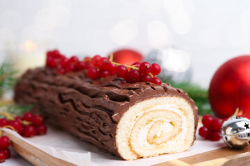 Delicious Yule log (traditional Christmas cake) with redcurrant, decor and fir tree branches on table, closeup