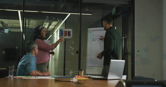 Professional woman highlighting printed chart against glass wall in conference room, with laptop - Powered by Adobe