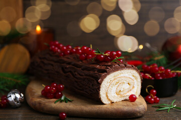 Delicious Yule log (traditional Christmas cake) with redcurrant on wooden table, closeup