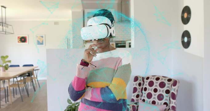Standing woman wearing VR headset and striped sweater in home living area, with wooden dining table