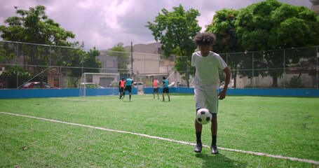African American Latin man performing kick-ups on soccer field during casual match, balancing soccer ball skillfully while teammates play behind