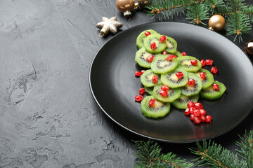 Christmas tree made of kiwi, pomegranate seeds and festive decor on black table, closeup. Space for text