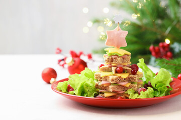 Christmas food. Fir tree made of bread, cheese, ham, lettuce and decor on white table against background with blurred lights, space for text. Bokeh effect