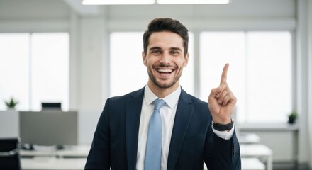 Fototapeta premium Cheerful man in suit points upwards, smiling in a bright office