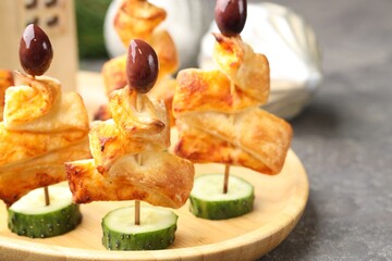Tasty snacks with puff pastry, olives and cucumber on grey textured table, closeup. Christmas appetizer