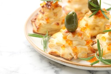 Tasty snacks with puff pastry, olives, red caviar and rosemary on white marble table, closeup. Christmas appetizer