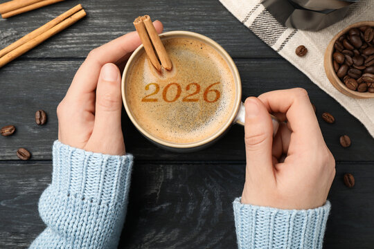 Hello New 2026 Year. Woman holding cup of coffee with numbers on black wooden table, top view