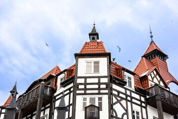 A cropped view of timber-framed building with red tiled roofs and wooden balconies stands against a bright blue sky, exuding European village charm and architectural detail.