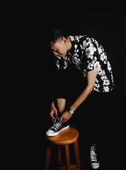 Asian Young Man Tying Sneakers While Sitting on Stool.  