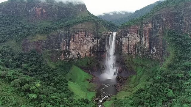 Ultra-wide aerial video of Angel Falls cascading down a multi-toned sandstone 'tepui' cliff, mist-shrouded, amidst pristine emerald Amazonian jungle. Awe-inspiring natural wonder