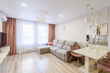 A stylish living room with a modern couch, dining area and elegant lighting. The space is bathed in natural light and features warm, inviting tones