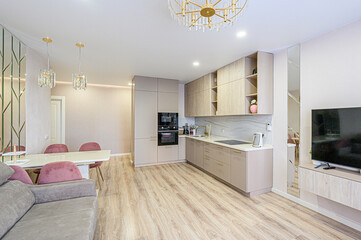 Modern apartment with open kitchen, dining area, and living room. Features include light wood floors, neutral tones, a crystal chandelier, and sleek cabinetry