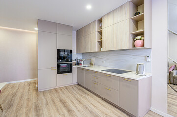 A modern kitchen with light wood flooring, neutral-toned cabinets with gold handles, built-in appliances, and open shelving. The design is clean and minimalist