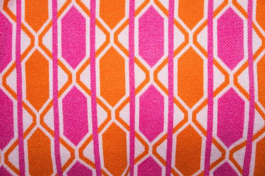 Bright, retro geometric knit fabric featuring a bold interlocking honeycomb or lattice pattern in vibrant pink, orange, and white. Perfect for 60s fashion, groovy backgrounds, or textile projects