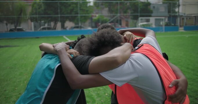 Hispanic friends in soccer huddle before game, arms around each other showing unity, motivation, and friendship, moment of teamwork, encouragement, and shared passion for sport