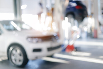Blurred view of auto repair shop with cars on hydraulic lifts, sunlight