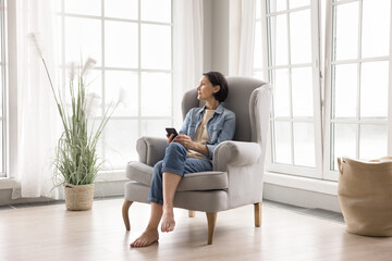 Calm pensive older woman spending time in armchair with phone
