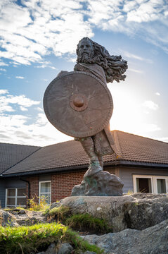 King Harald, Fairhair statue, bearded warrior holding a shield stands in front of a house with a cloudy sky, sunbeam, vertical shot, Haugesund, Norway