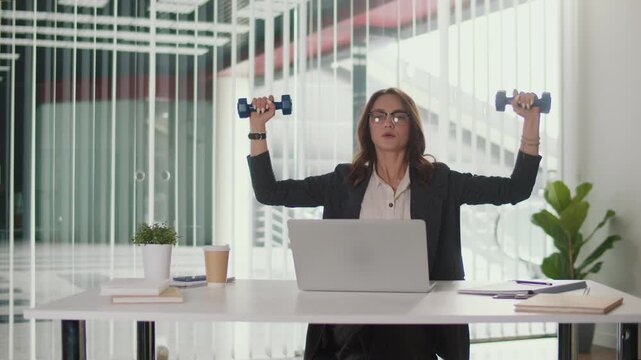 Office Ergonomics and Employee Wellbeing. Office Manager Performs Shoulder and Upper Spine Exercise with Dumbbells at Desk to Improve Posture, Prevent Pain, Support Productivity and Corporate Wellness